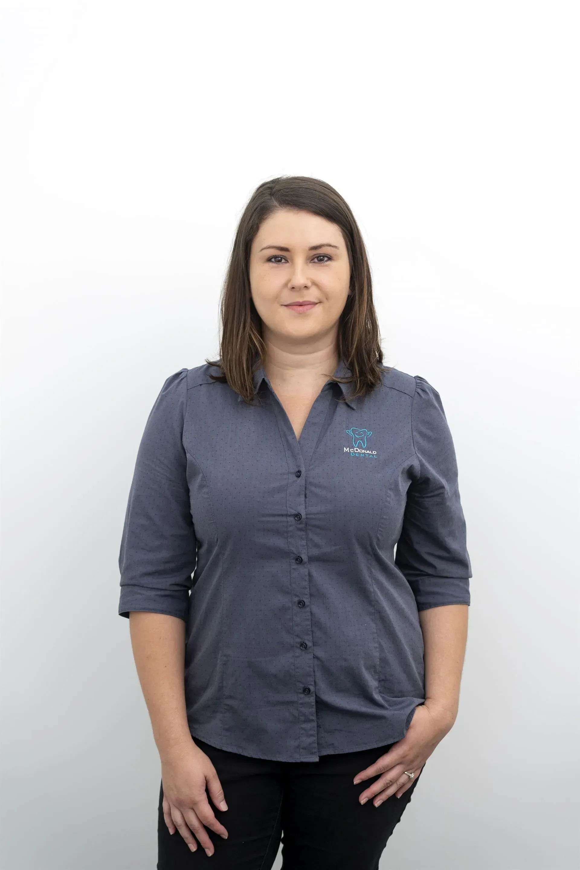 Woman in a blue button-down shirt and black pants, standing against a white background. — McDonald Dental in Gympie, QLD