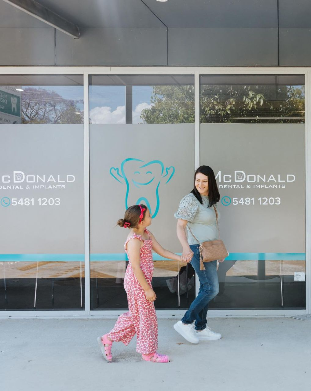 A Woman and Child Walking Past a Dental Office With a Blue Tooth Logo — McDonald Dental in Gympie, QLD