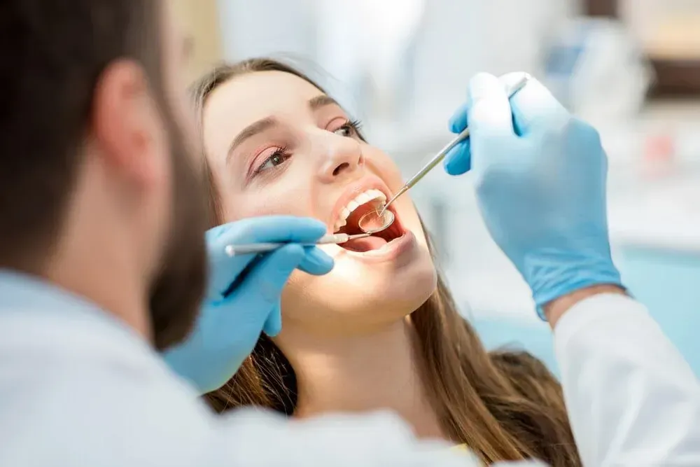 Dentist examining a patient's teeth with dental instruments; blue gloves, bright light. — McDonald Dental in Gympie, QLD