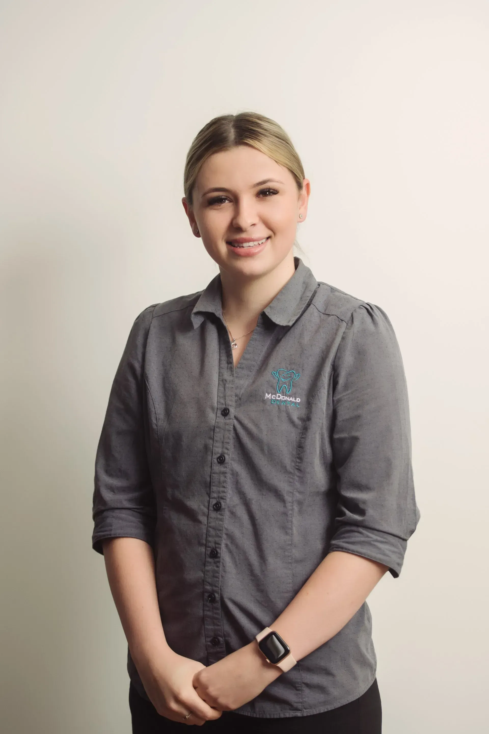 Woman in gray shirt smiles, arms crossed, stands against a white background. — McDonald Dental in Gympie, QLD