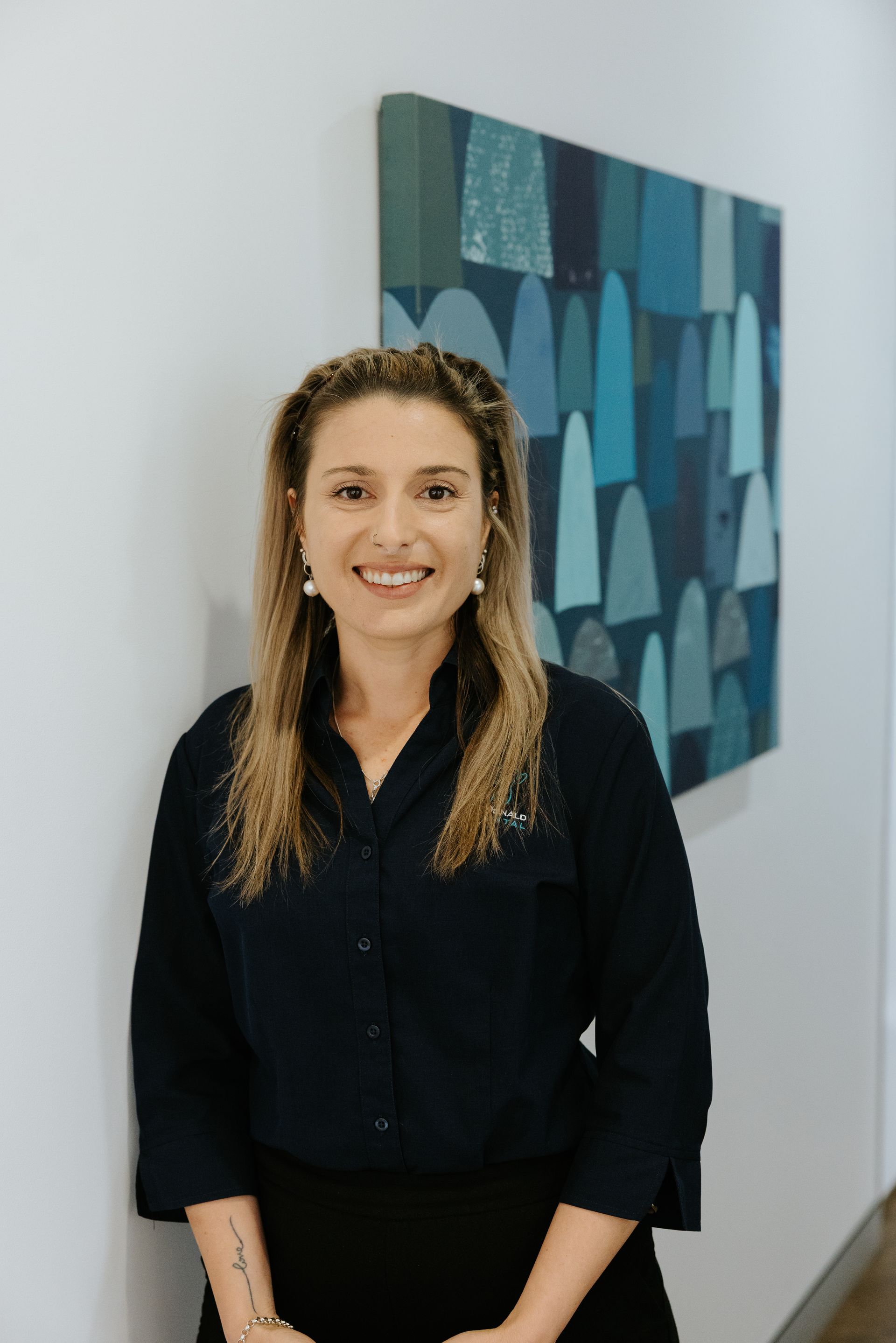 Woman in gray button-down shirt smiles, arms crossed, in front of a neutral background. — McDonald Dental in Gympie, QLD