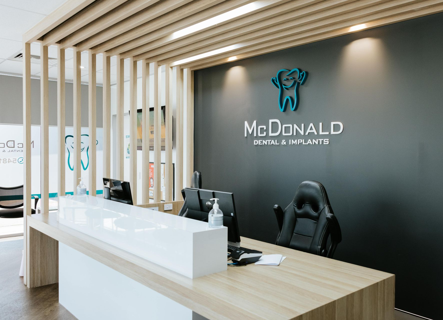Reception area of McDonald Pediatric Dentistry. White and wood desk, black accent wall with logo, and a black chair. — McDonald Dental in Gympie, QLD