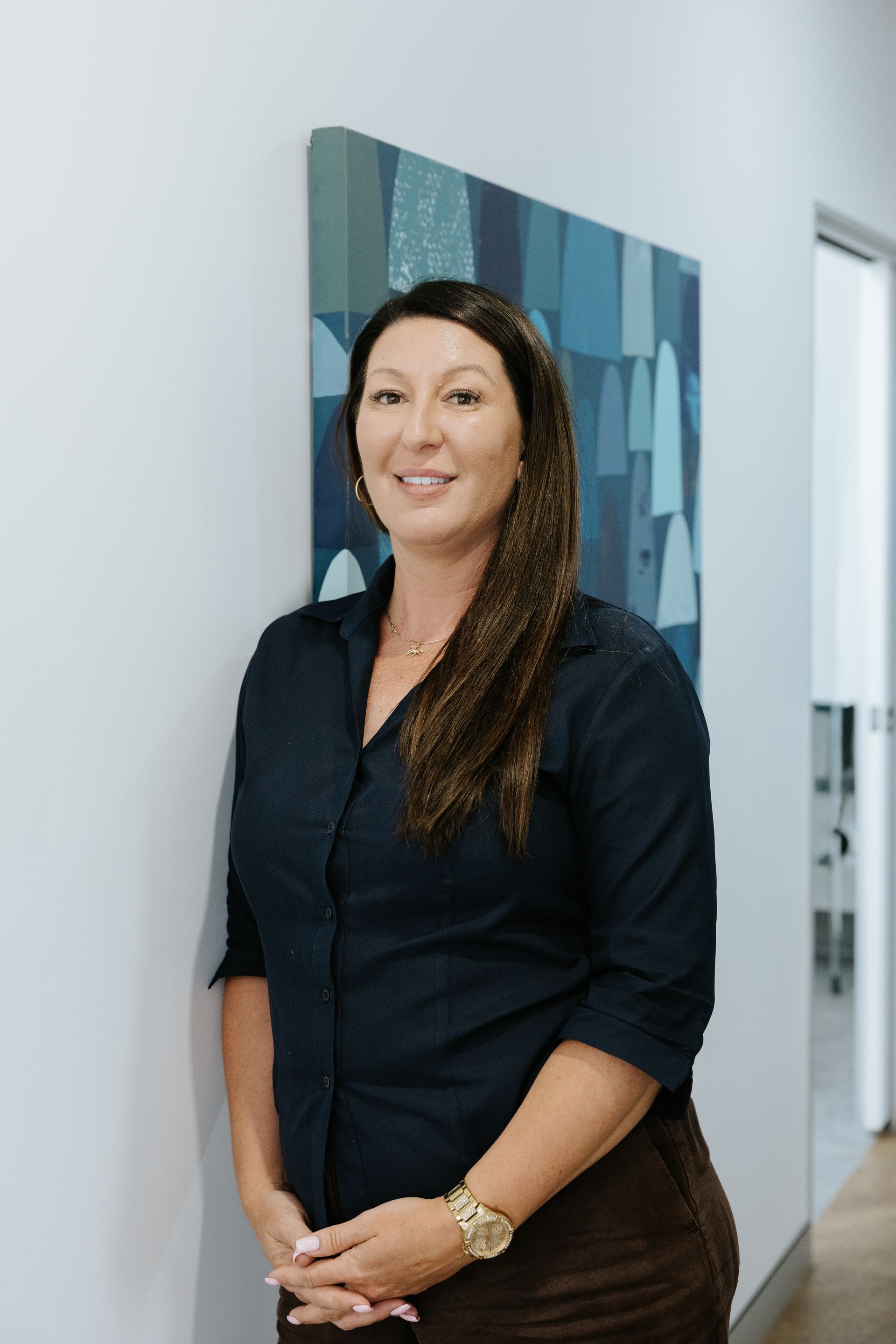 Woman in gray scrubs smiles, hands in pockets. Light blue trim and logo on top. White background. — McDonald Dental in Gympie, QLD