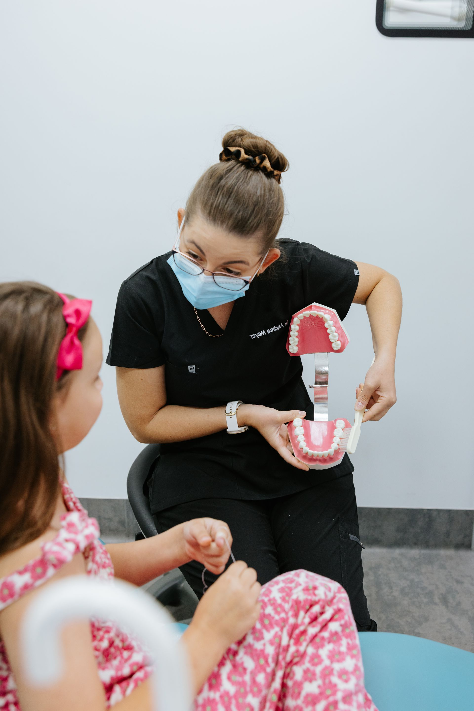 Dentist showing a young patient a dental model. Both seated in a dental office. The dentist is wearing a mask and dark scrubs. — McDonald Dental in Gympie, QLD