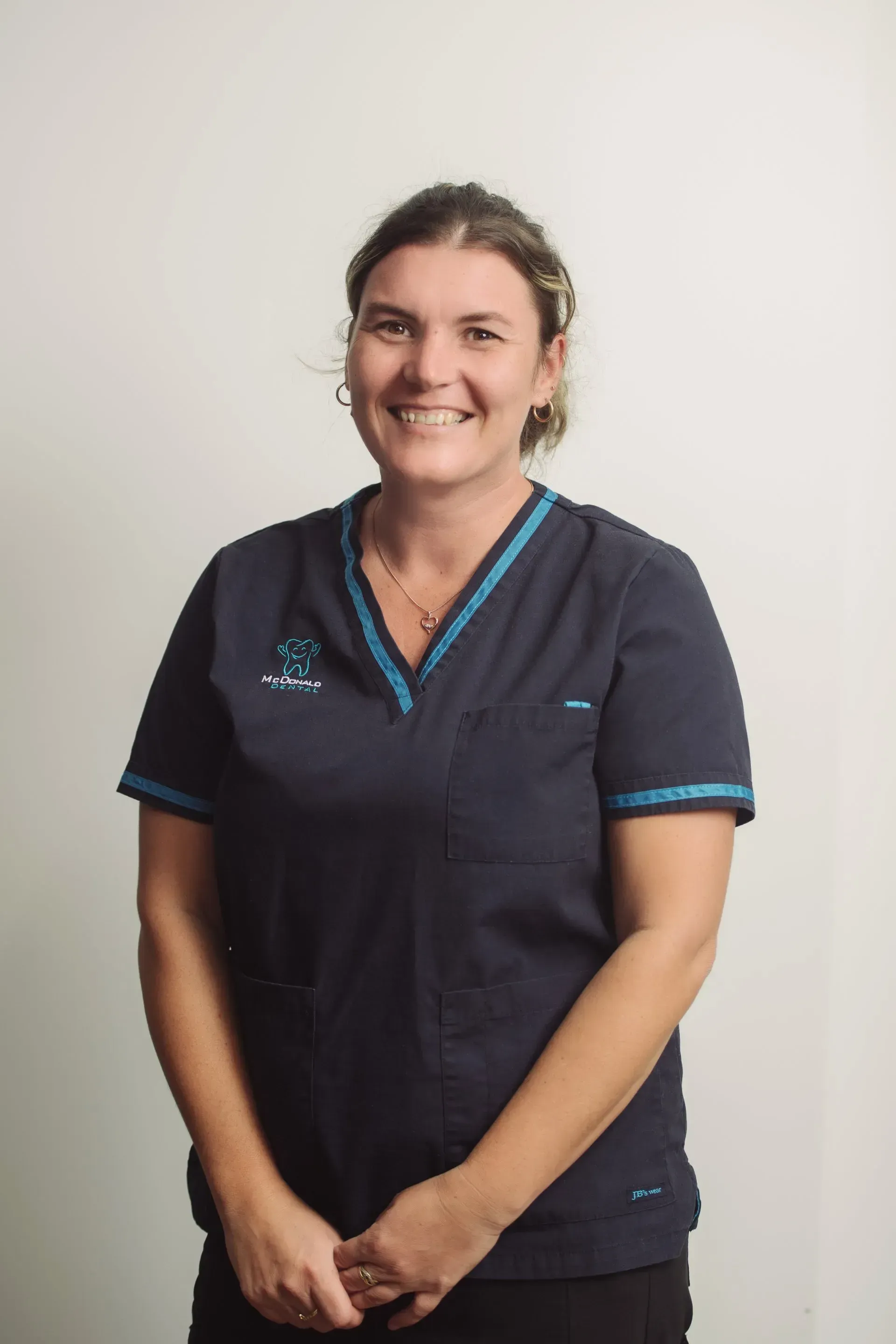 Woman in navy scrubs smiles, standing against a white wall. — McDonald Dental in Gympie, QLD