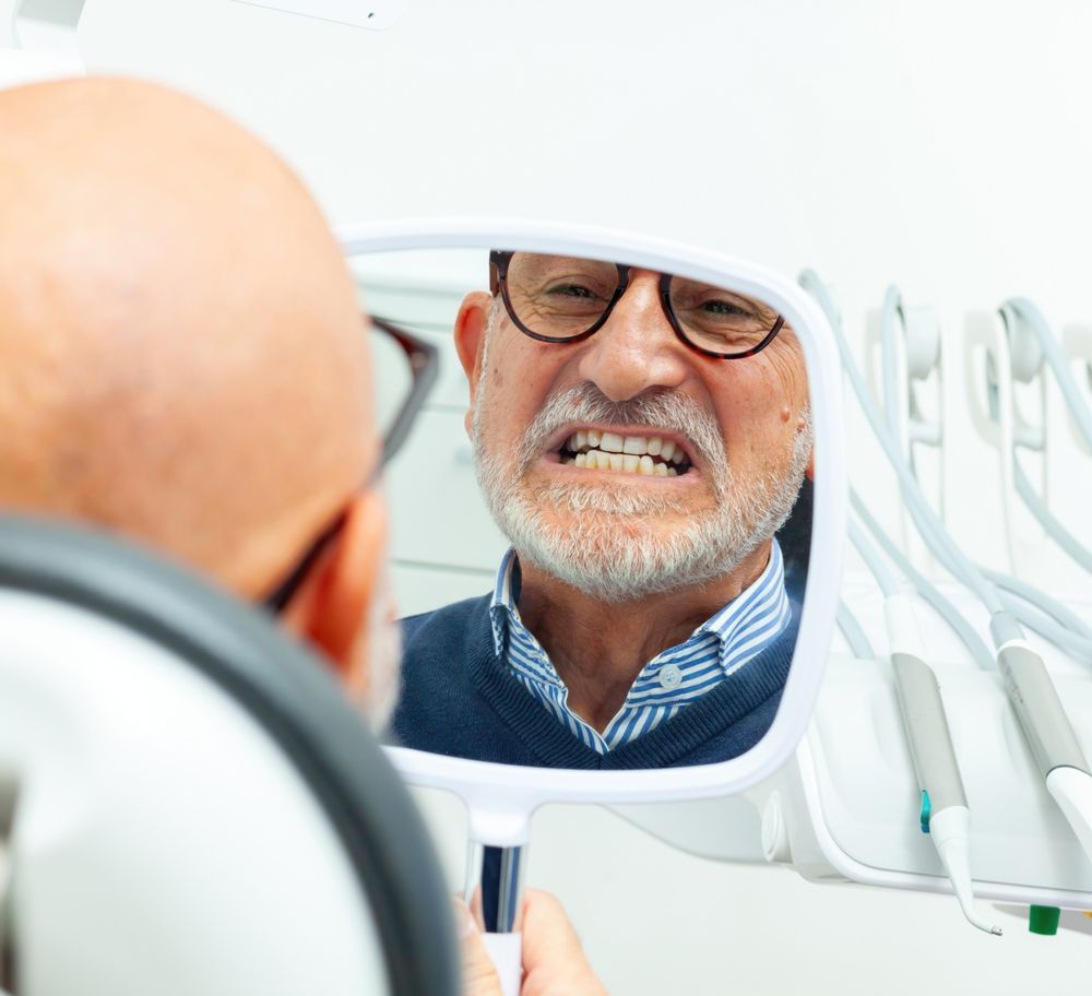 Man in glasses looking at his teeth in a mirror at a dentist's office. — McDonald Dental in Gympie, QLD