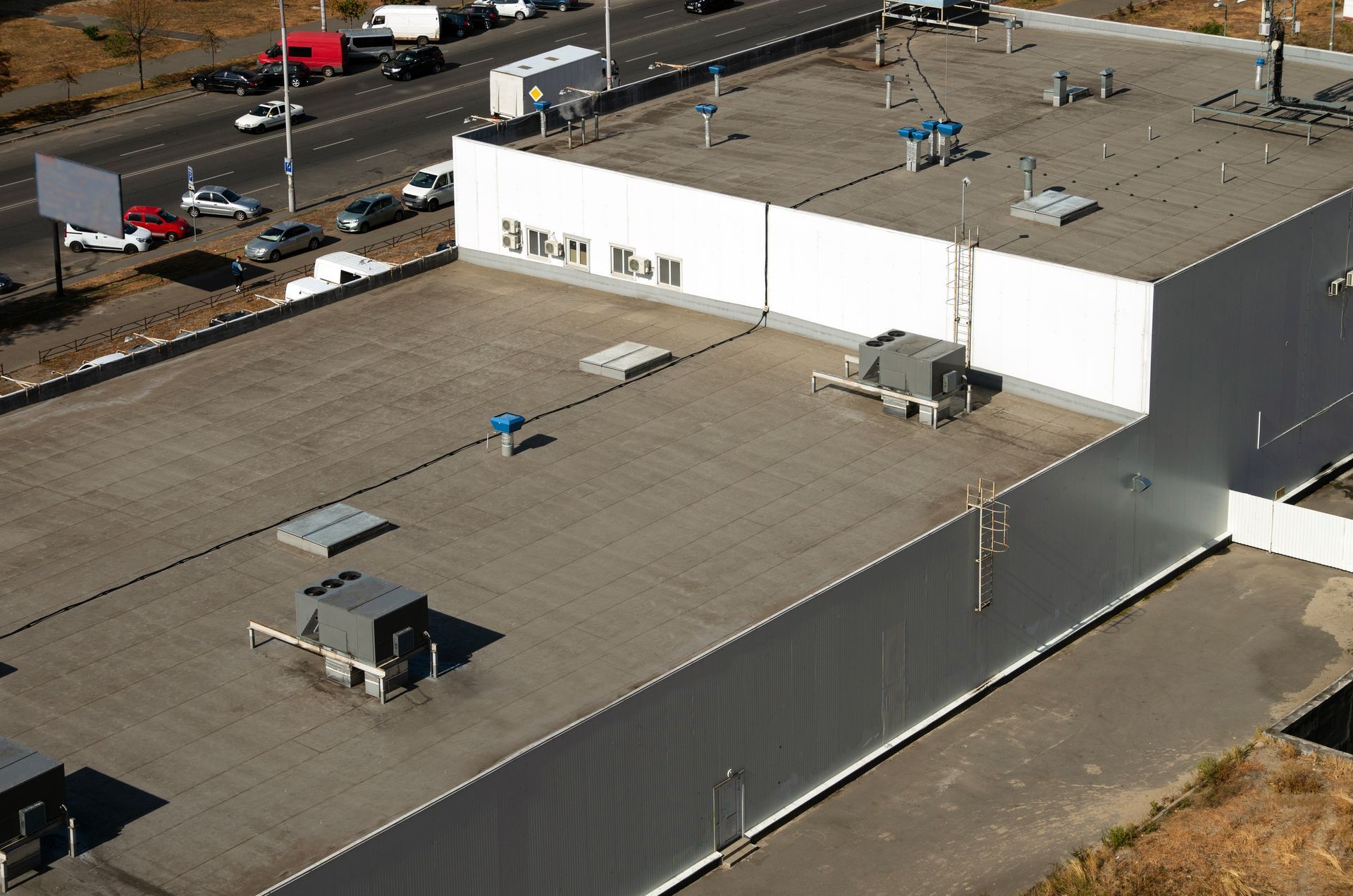 Aerial view of a large flat commercial roof with vents and equipment along a busy road.