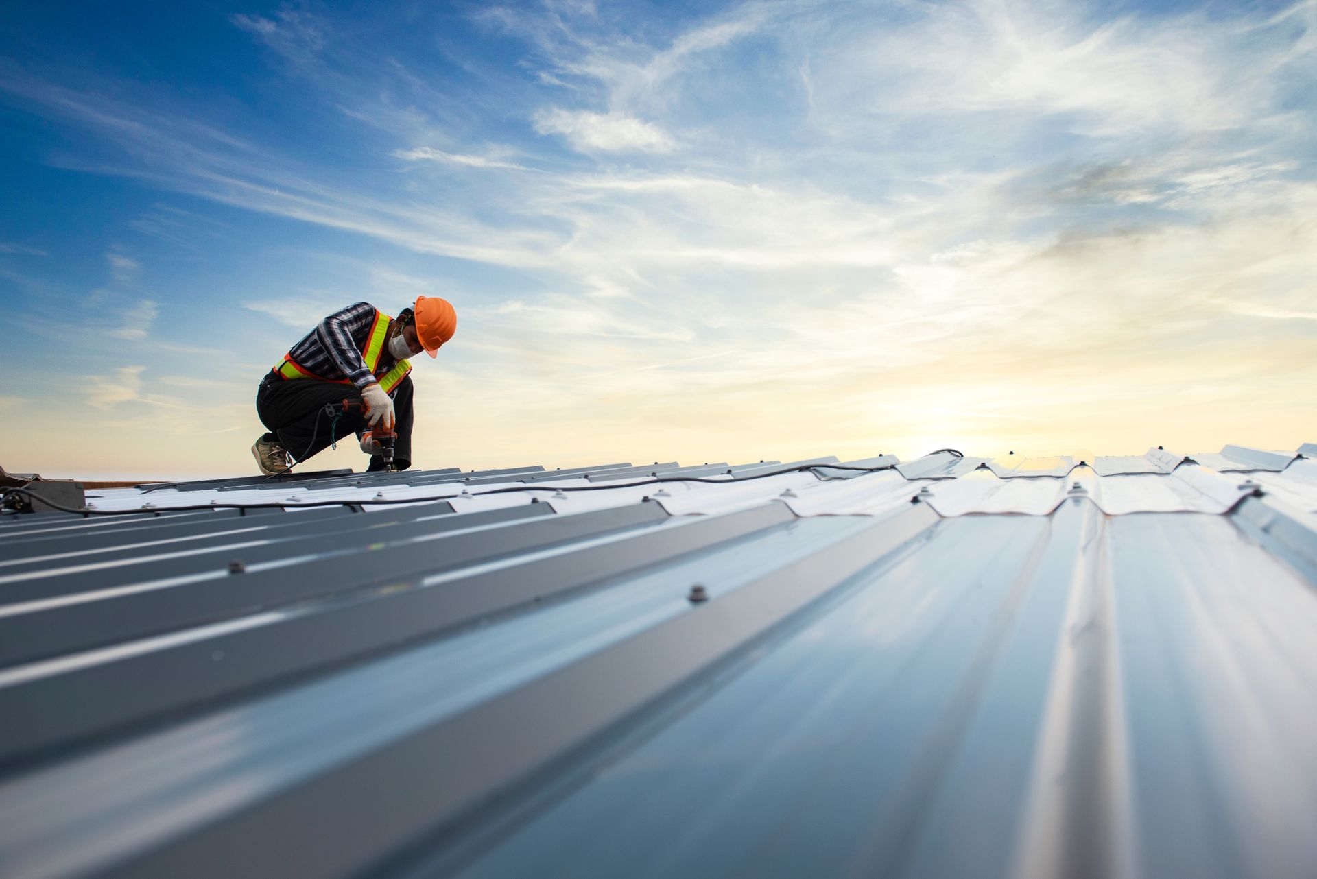 Worker installing a metal commercial roof under a bright sky at sunset.