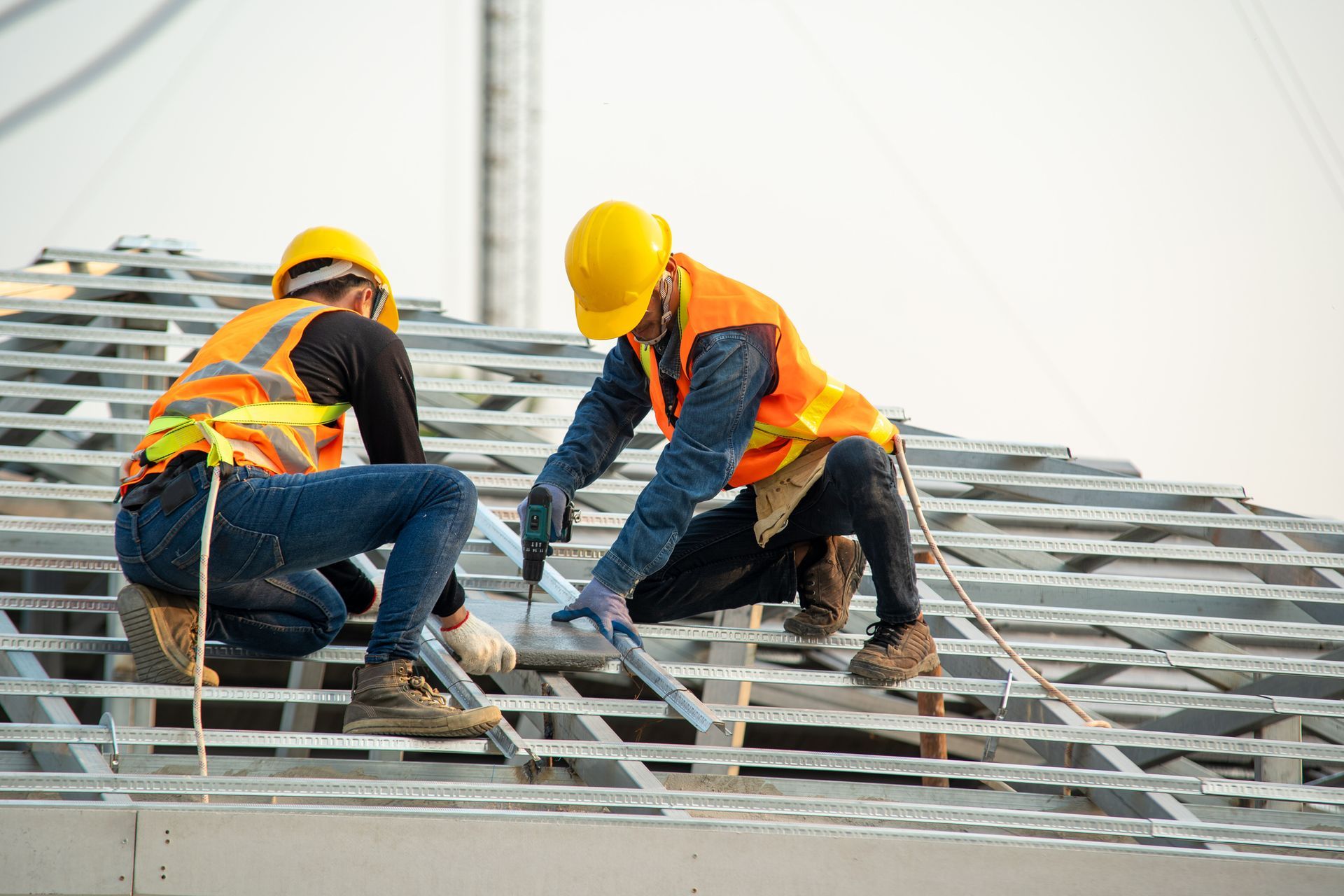 Two workers on a roof, wearing helmets and safety vests, installing commercial roofing.