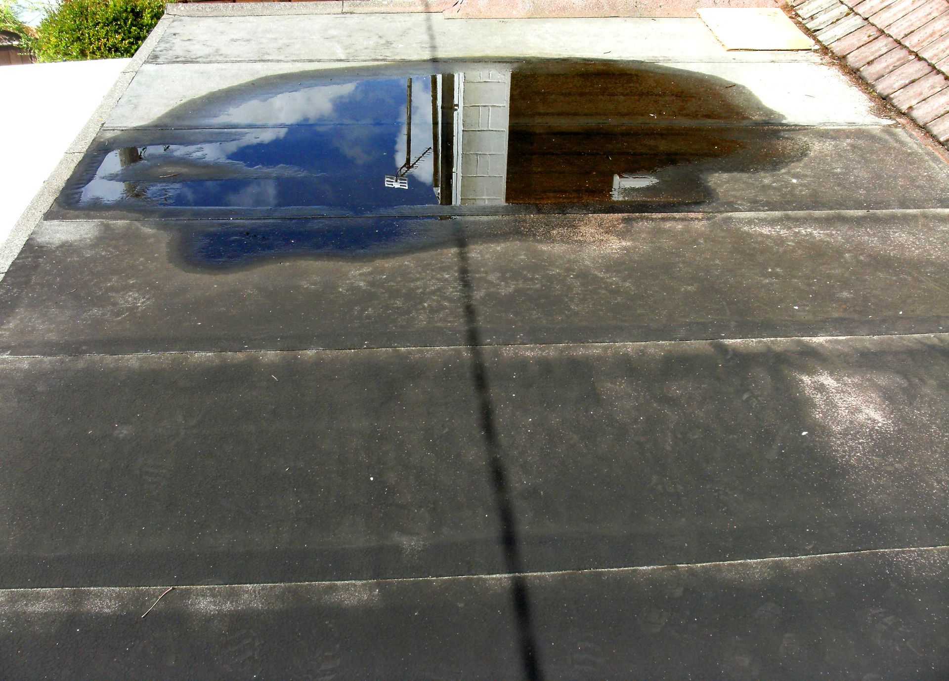A puddle lies on top of an asphalt flat roof.