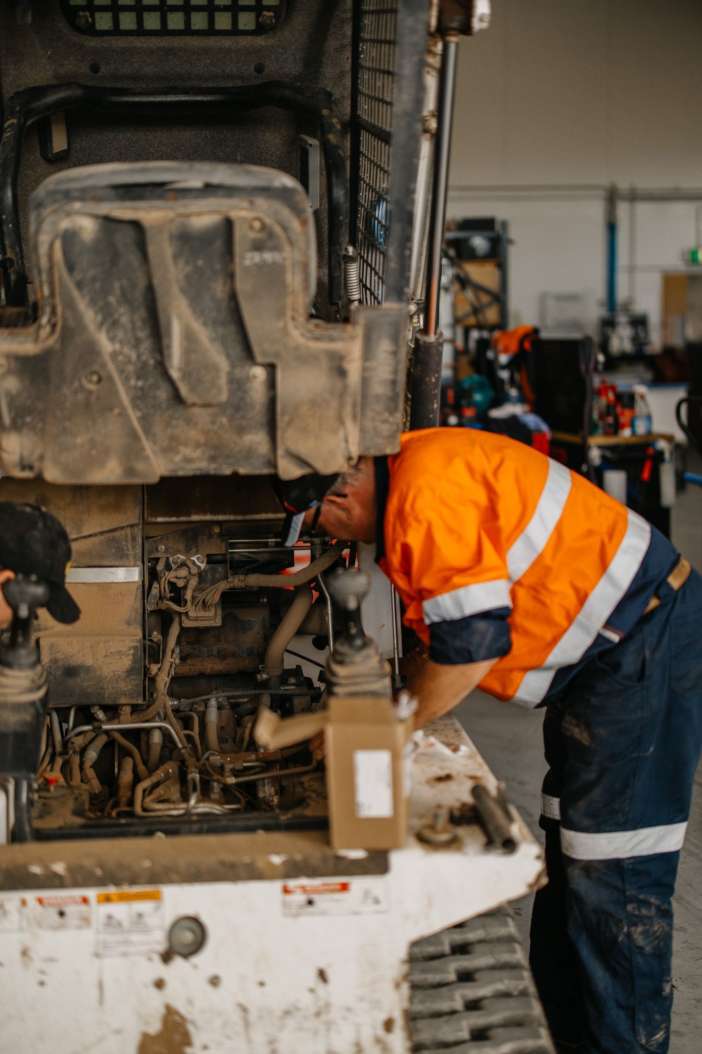 Worker in orange safety vest inspecting machinery in a workshop.