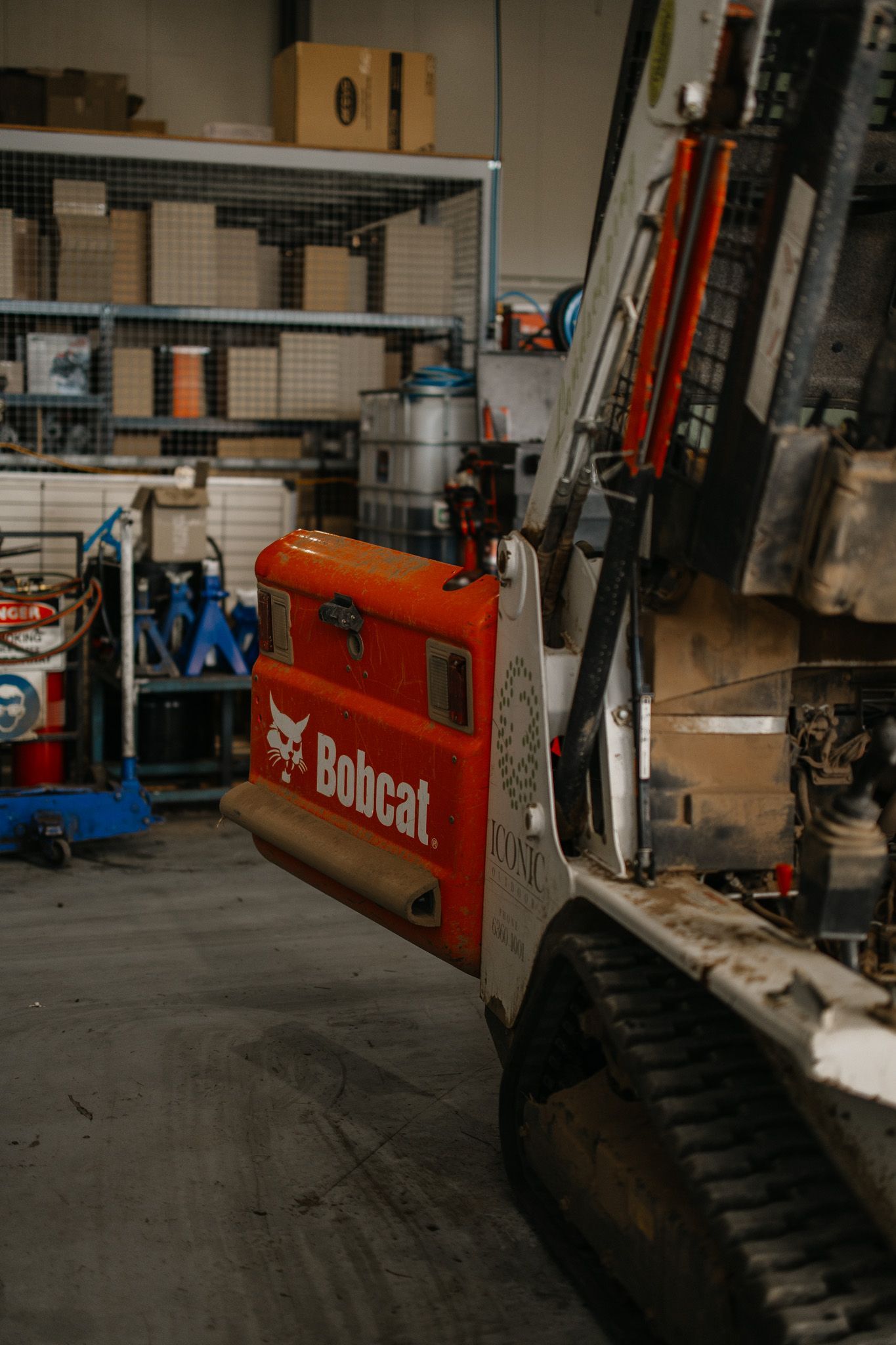 Bobcat machinery with its side door open in a workshop. Red and white with visible tracks and boxes on shelves.