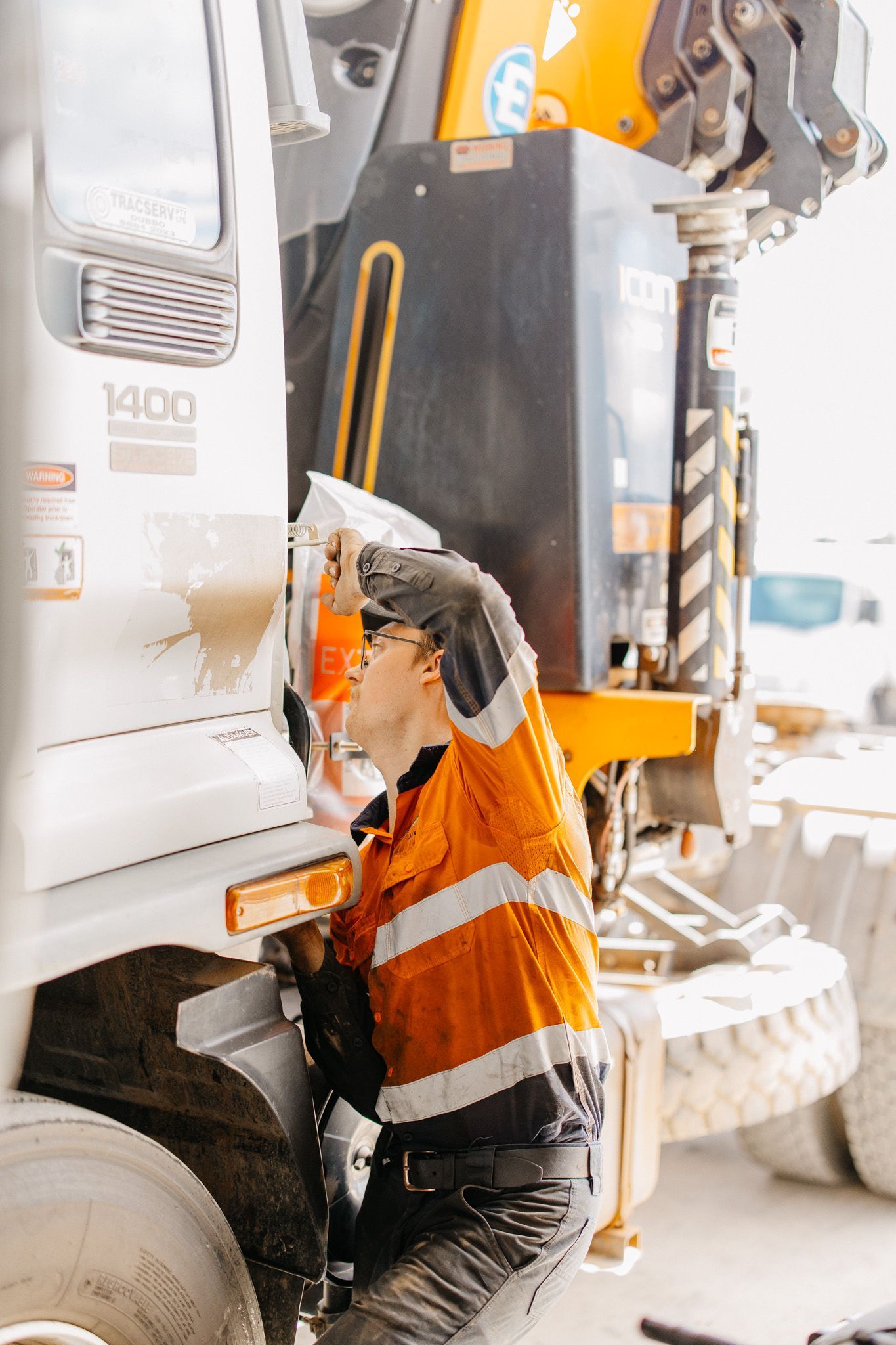 Person in safety vest working on machinery near a truck.