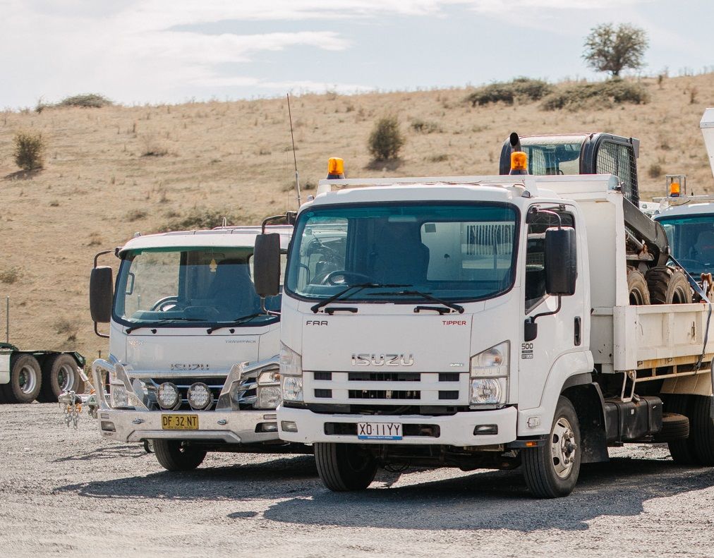 White Isuzu trucks parked in a lot, with a dry, hilly background.
