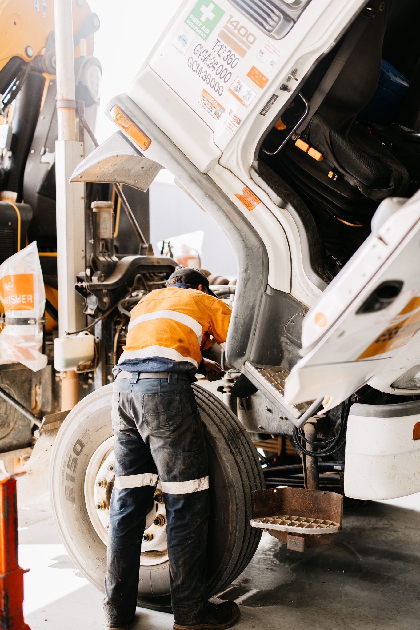 Mechanic in orange vest working on truck tire, hood open.