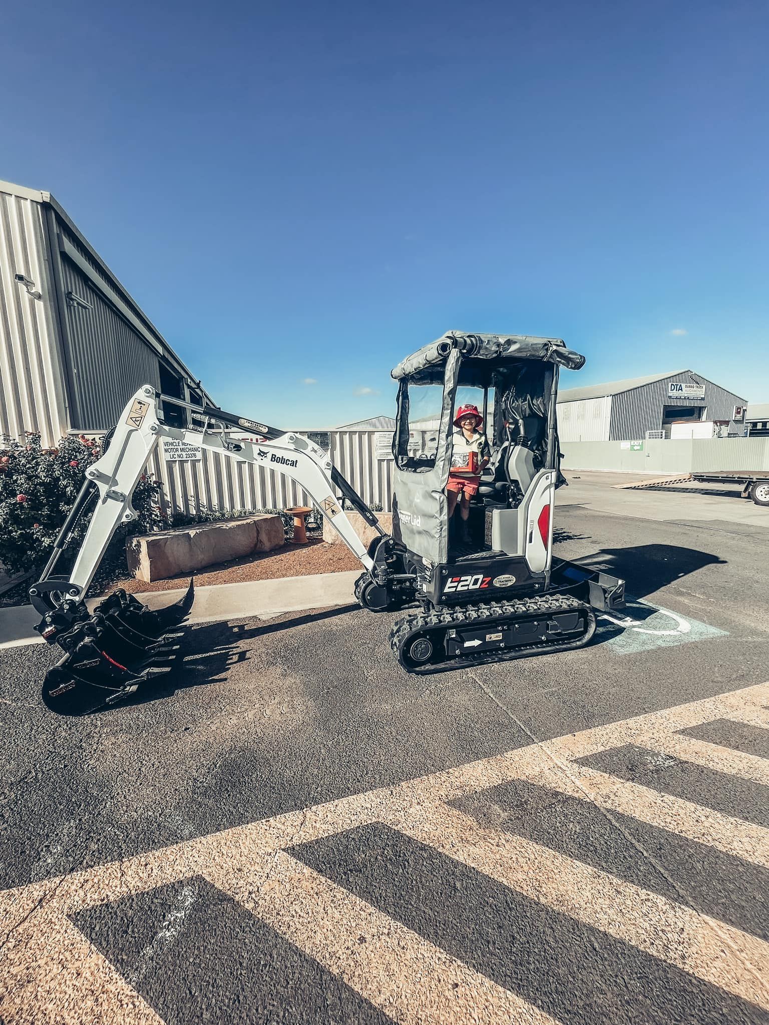 A Man Is Driving A Small Excavator In A Parking Lot — Tracserv in Mudgee, NSW