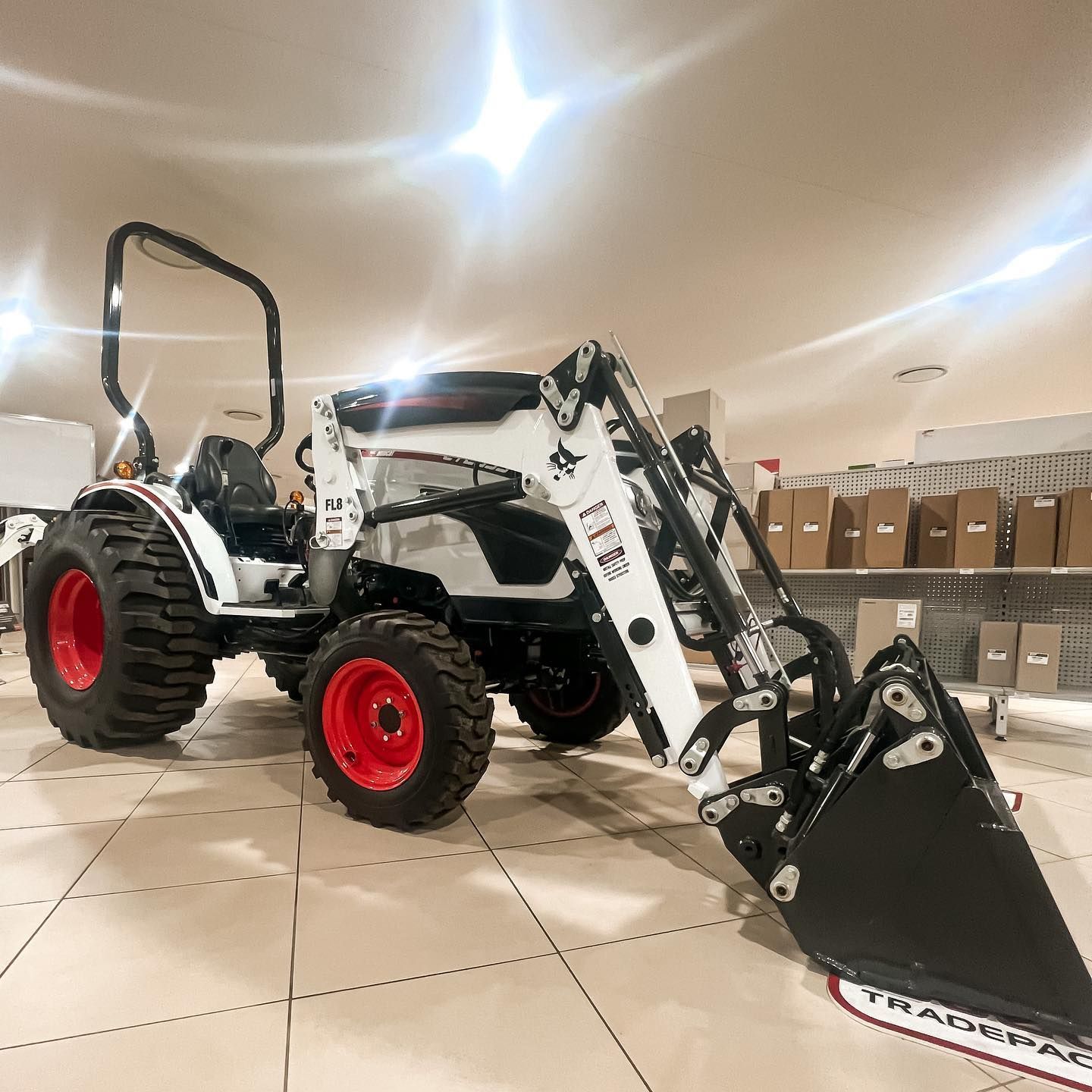 White Bobcat tractor with a black bucket and red wheels in a store.