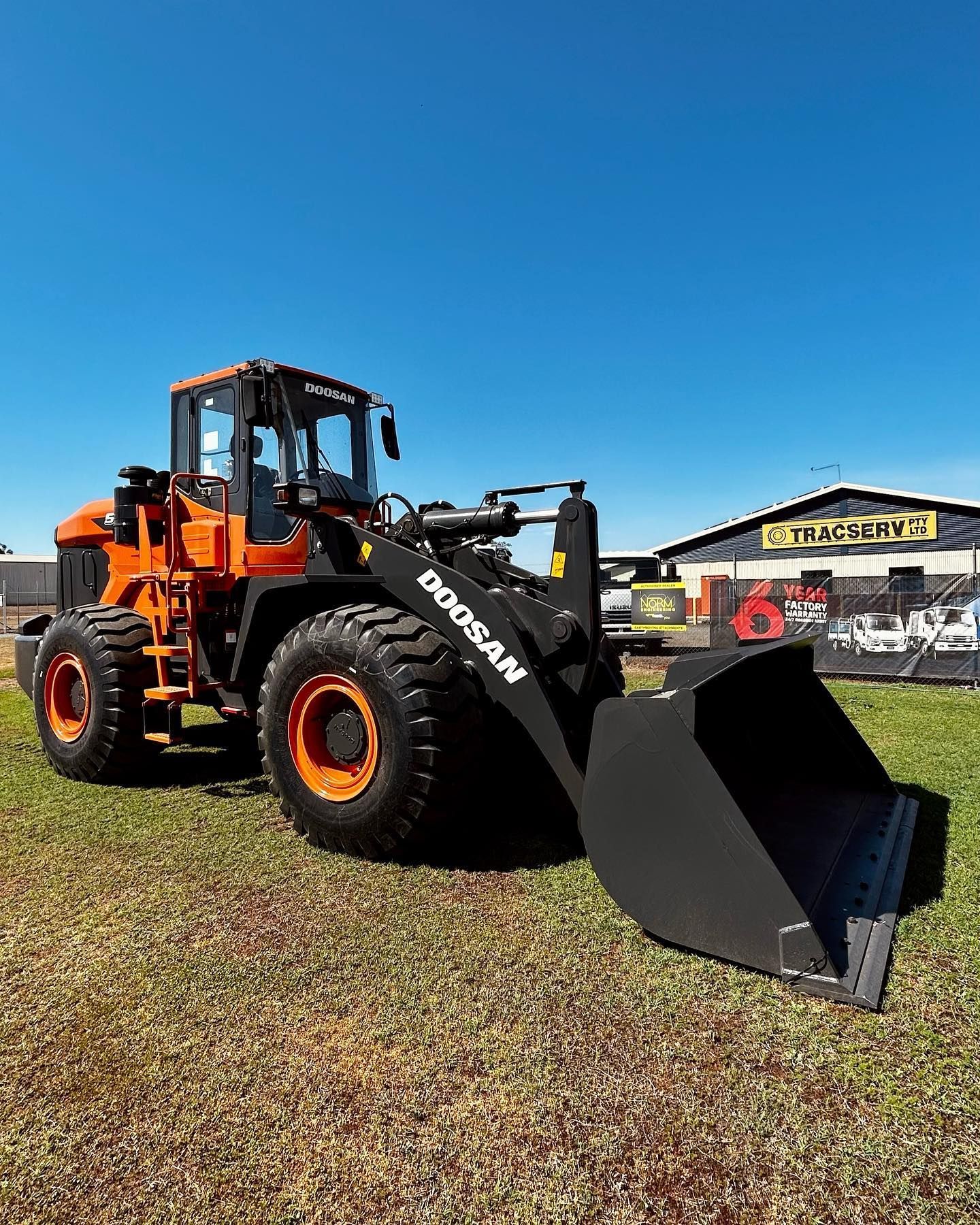 A Bulldozer Is Parked In A Grassy Field In Front Of A Building — Tracserv in Parkes, NSW