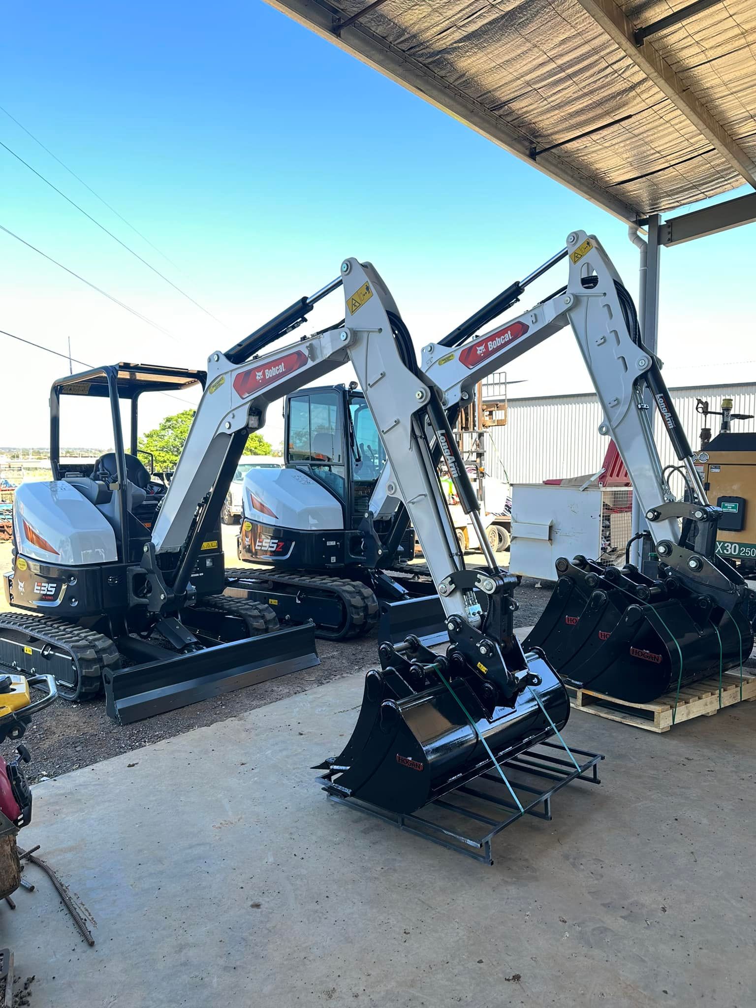 Two excavators are parked next to each other under a canopy.