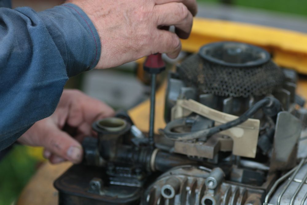 A Man Is Working On A Lawn Mower Engine With A Screwdriver — Tracserv in Dubbo, NSW
