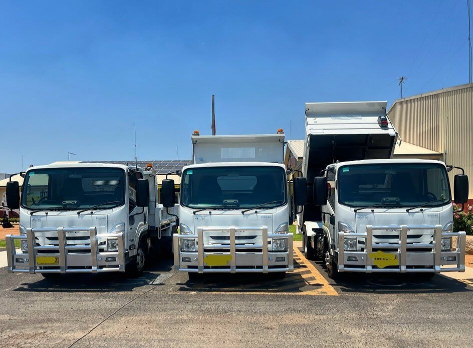 Three white dump trucks parked outside on a sunny day. One bed is raised.