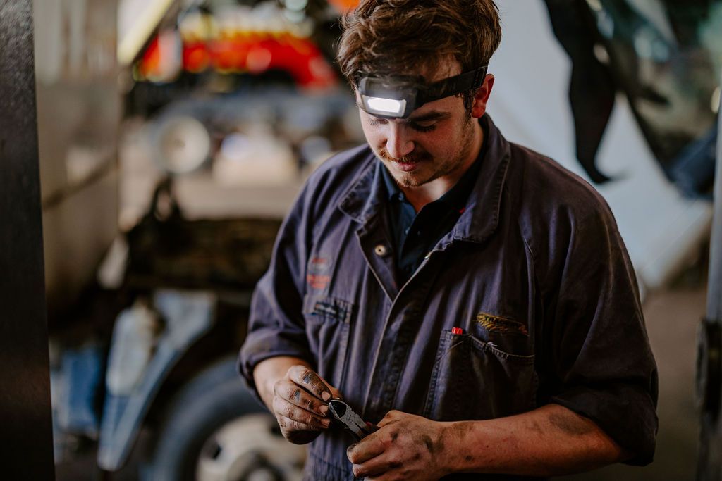 A Man Wearing A Headlamp Is Working On A Car In A Garage — Tracserv in Dubbo, NSW