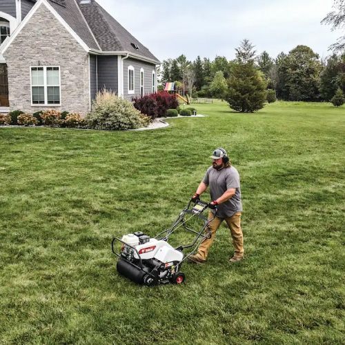 Man Mowing a Green Lawn with A Walk-Behind Lawnmower in Front of A Gray House — Tracserv in Dubbo, NSW