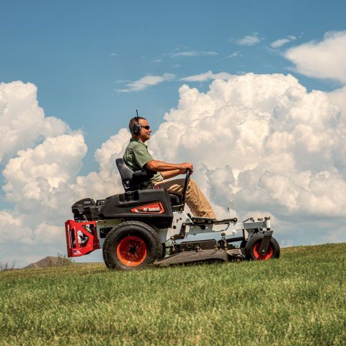Man Operating a Bobcat Zero-Turn Mower on A Grassy Hill Under a Cloudy Blue Sky — Tracserv in Dubbo, NSW