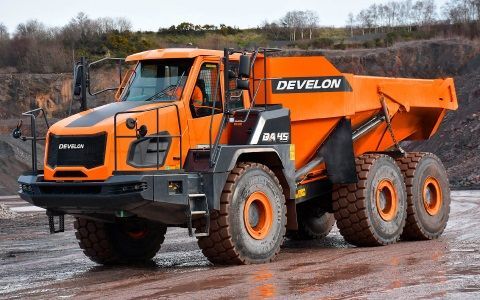 A large orange dump truck is parked in a dirt field.