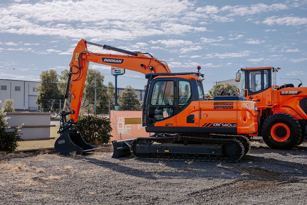 A Large Orange Excavator Is Parked Next To A Tractor In A Gravel Lot — Tracserv in Bourke, NSW
