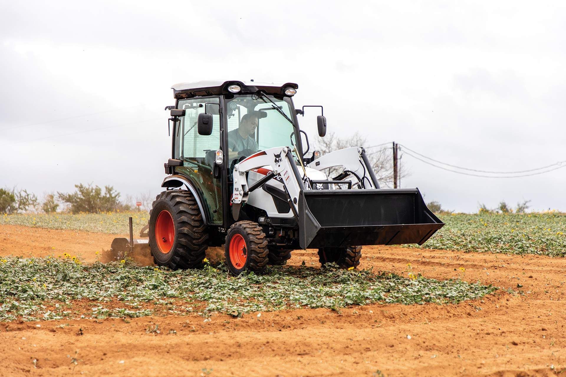 A Small Tractor With A Bucket Attached To It Is Driving Through A Field — Tracserv in Mudgee, NSW