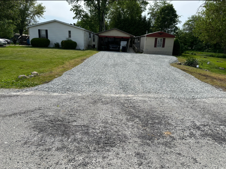 A gravel driveway leads to three mobile homes on a sunny day. Green grass and trees surround the homes.