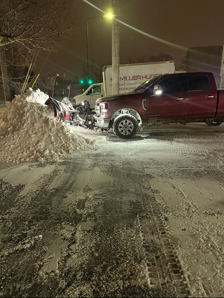 Red pickup truck with snowplow clearing snow at night. A large pile of snow is on the left.