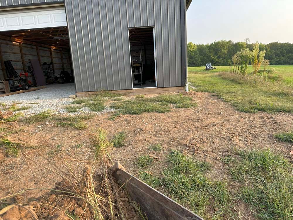 A gray metal building with an open door and gravel driveway next to grassy field.
