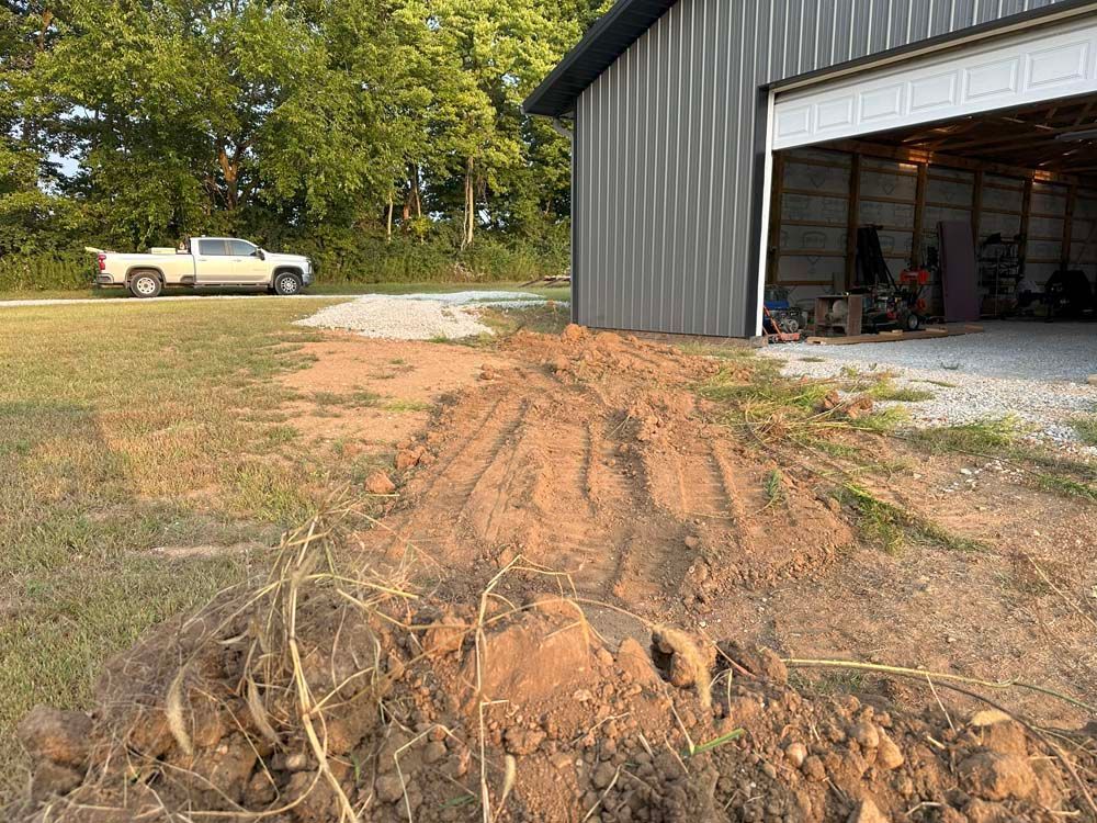 Muddy area near a metal garage. A pickup truck is parked nearby on a gravel drive.