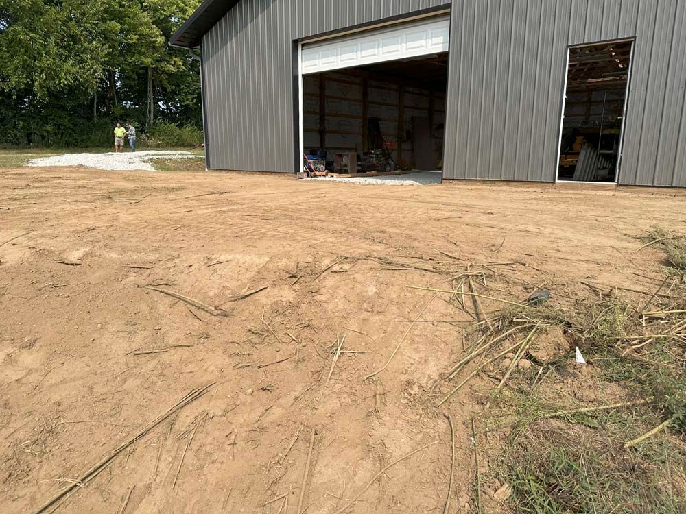 Dirt area in front of a gray metal building with an open garage door. Two people in the background.