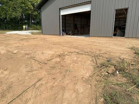 Dirt area in front of a gray metal building with an open garage door. Two people in the background.