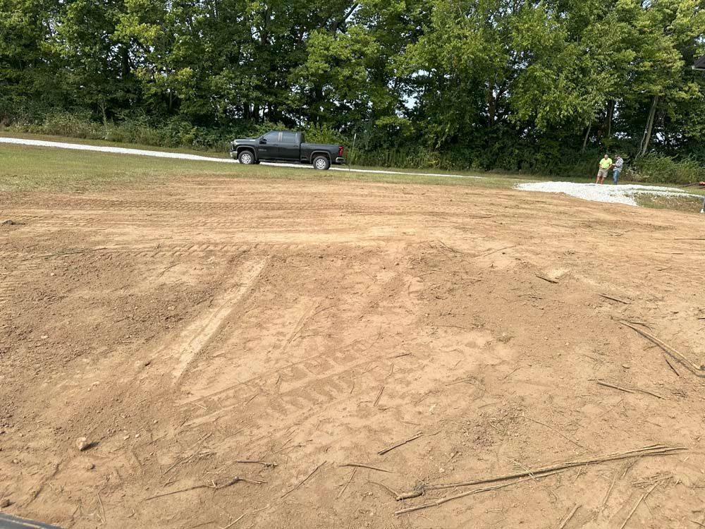 Dirt lot with dirt mounds, a black pickup truck, and workers by trees.