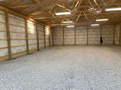 Inside of an empty open-air barn, gravel floor, wood framing, insulation.