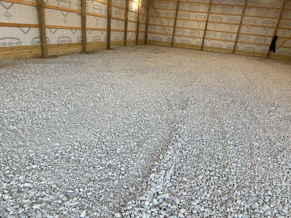 Interior view of a building with a gravel floor. Beige wooden beams line the walls.