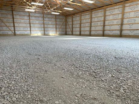 Gravel-covered interior of a large, empty, wood-framed building with bright overhead lighting.
