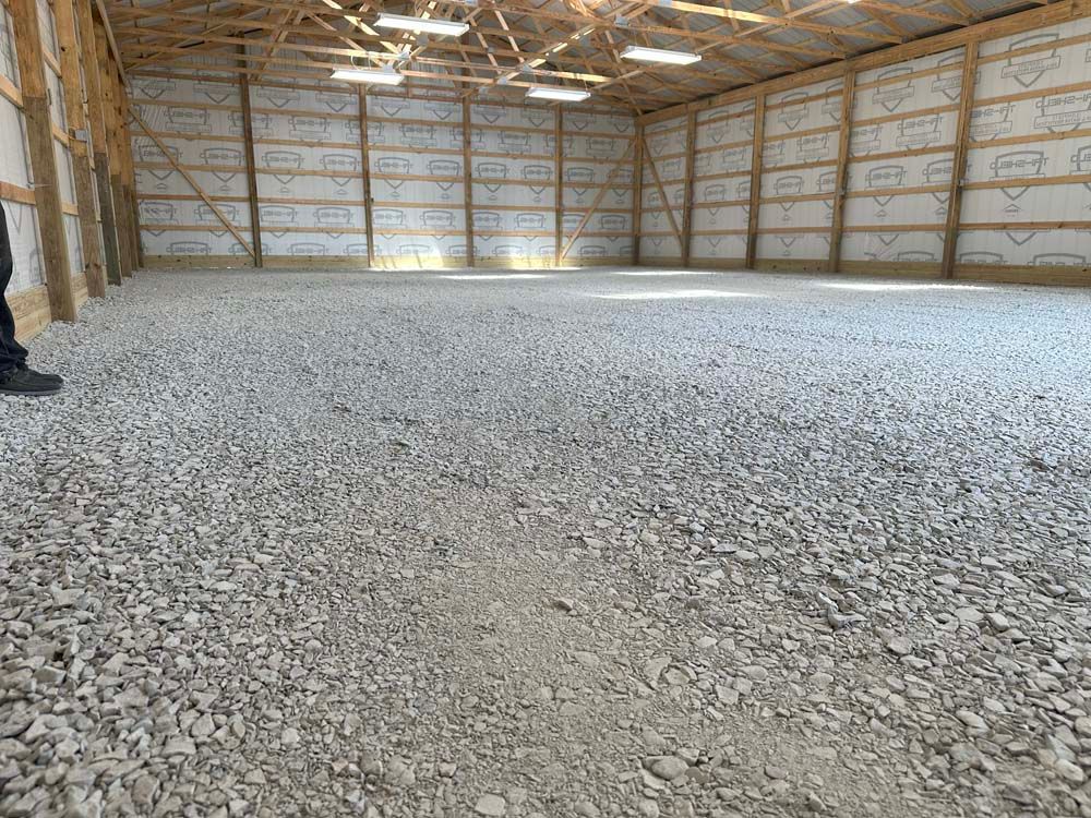 A large, empty barn with a gravel floor. Walls are lined with insulation, and the roof has exposed beams.