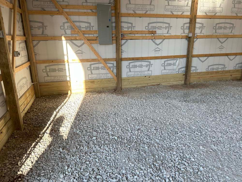 Interior of a new garage with gravel floor, wooden frame, and electrical panel on the wall.