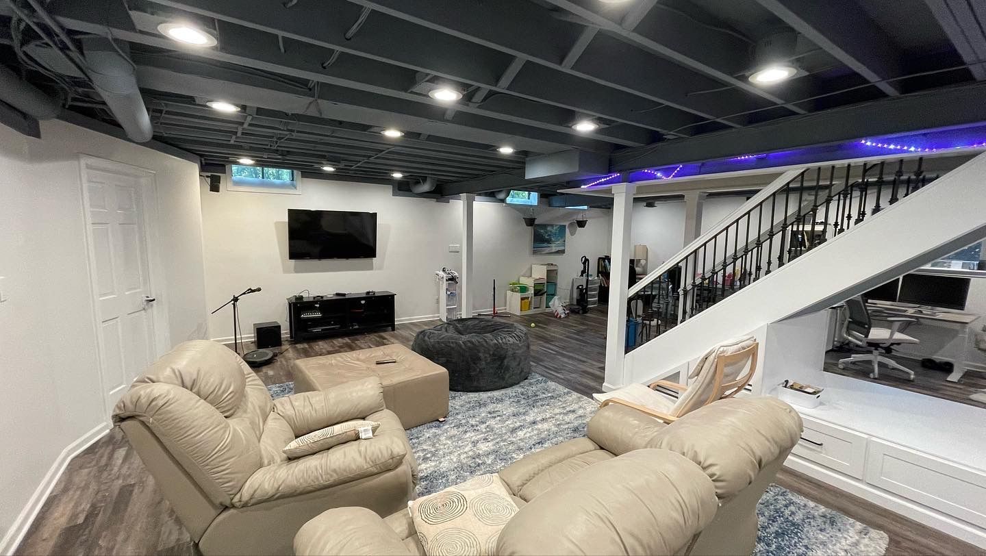 a basement living room with a couch , chairs , stairs and a flat screen tv .