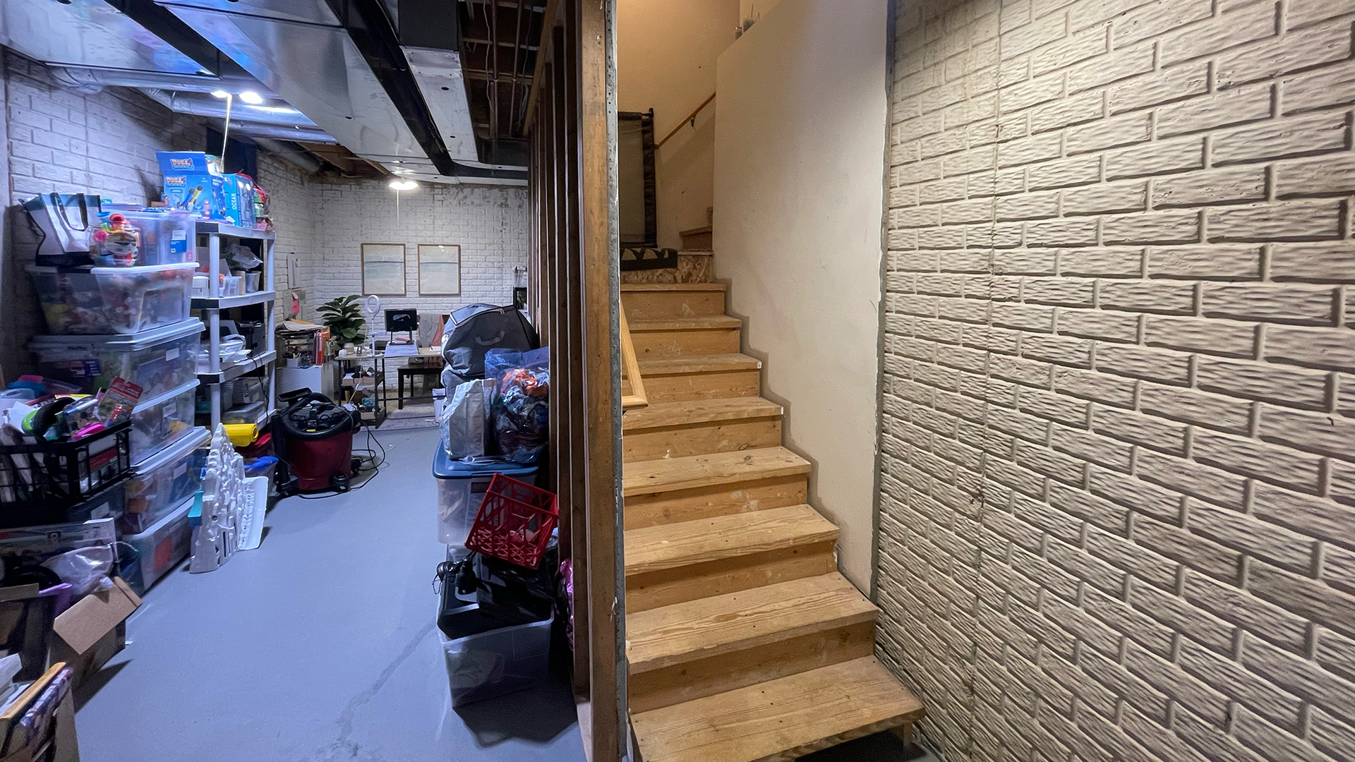 A basement with stairs leading up to the second floor and a brick wall.