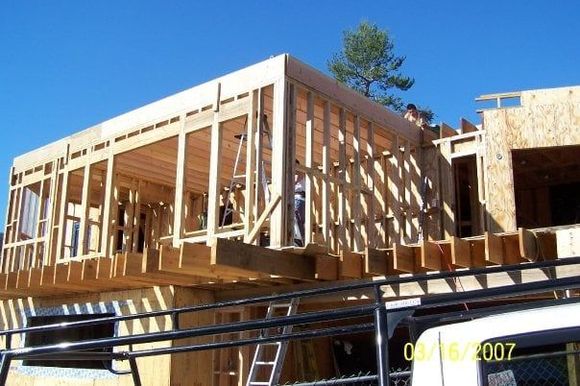Wood frame construction of a house; workers on the roof, clear blue sky.