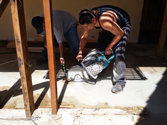 Two men cutting concrete with a saw outside, one using the saw, the other assisting.