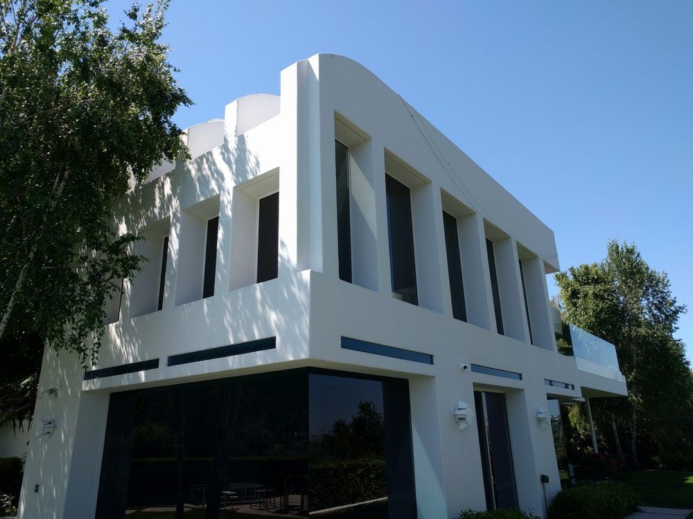 Modern white building with large dark windows, surrounded by trees.