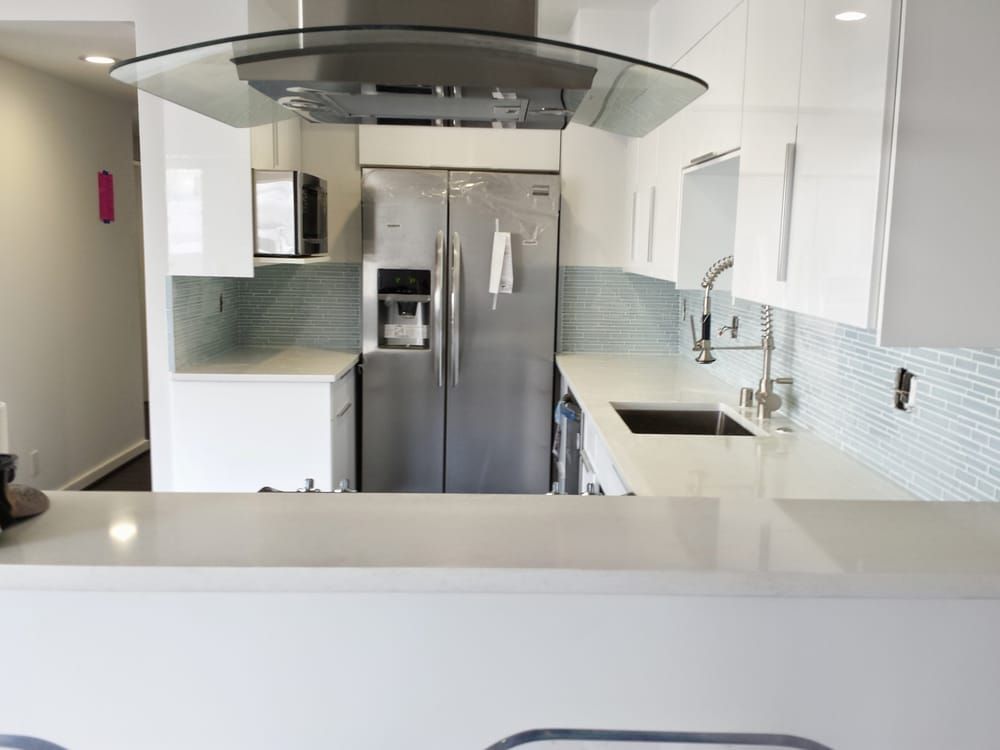 Modern kitchen with white cabinets, stainless steel appliances, and blue tile backsplash.