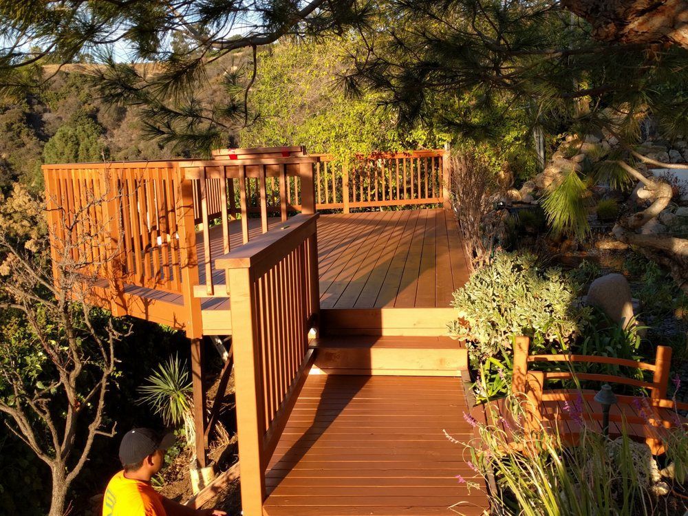 Wooden deck with railing overlooking lush greenery; a person in yellow shirt stands nearby.